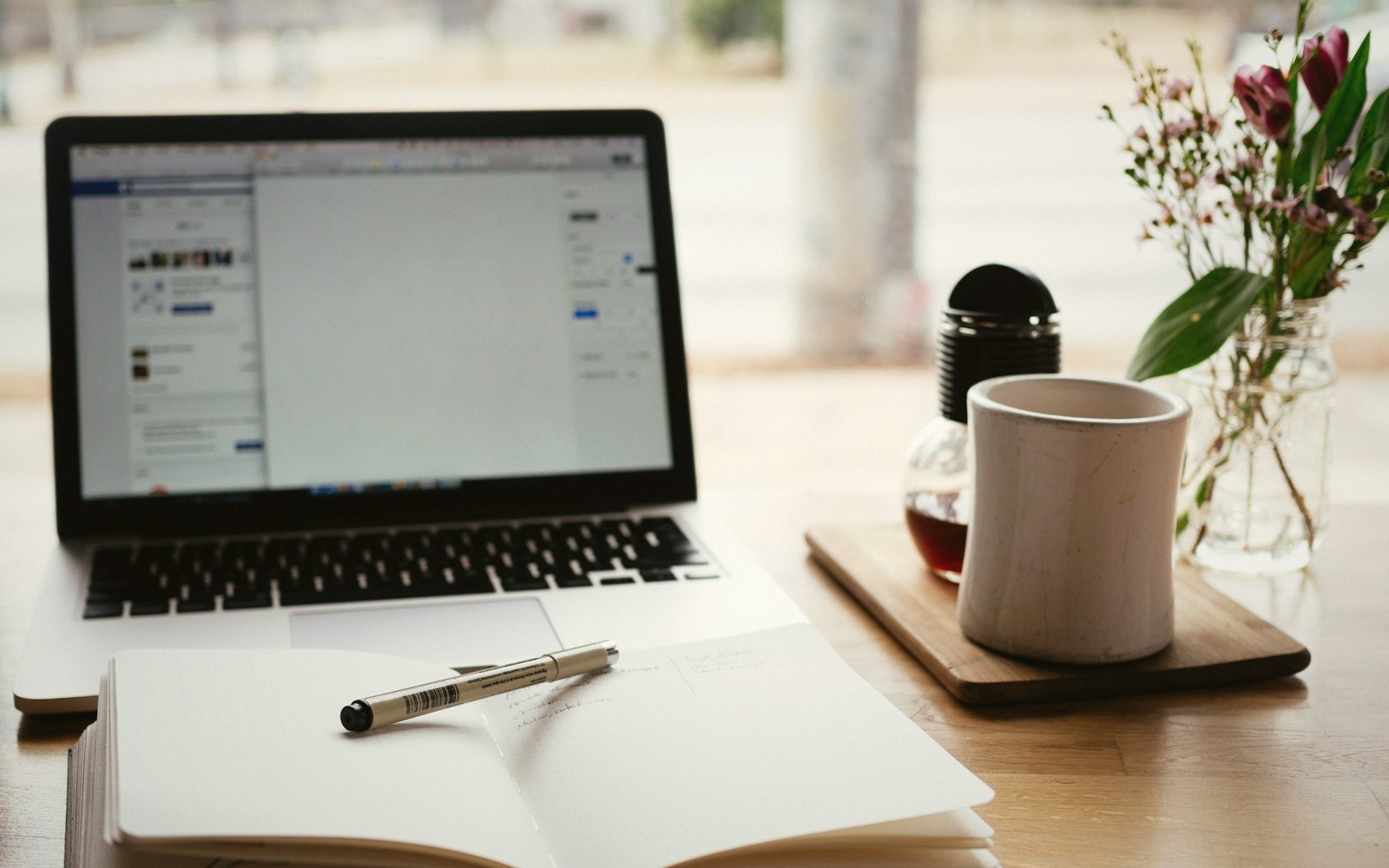 A stack of hardback books beside a spiral notebook and pen