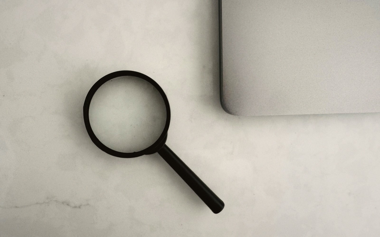A magnifying glass resting beside a closed laptop on a pale desk