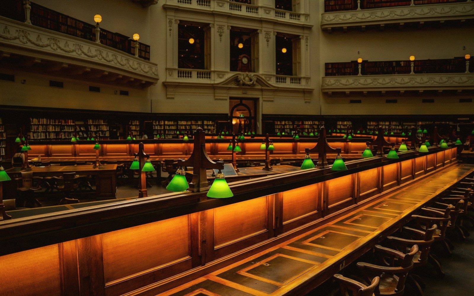 A grand library reading room with rows of desks and green-shaded lamps